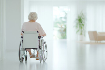 A serene image of an elderly woman sitting in a wheelchair being pushed by a nurse in a bright, peaceful healthcare environment. The space is filled with natural light and supportive care.