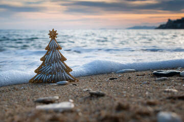 Christmas tree on sandy beach, sea waves and sunset seascape on background. Happy New Year and Merry Christmas travel destinations, celebration holidays in warm countries