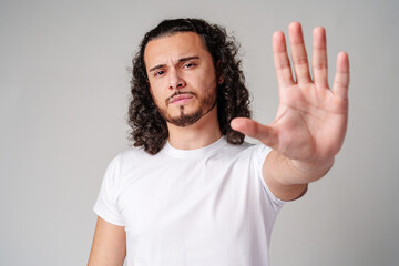 Fototapeta premium Young man with curly hair gestures to stop while wearing a plain white t-shirt against a neutral background