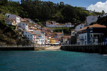 A picturesque coastal village nestled on a hillside, with colorful houses cascading down to the waterfront. The crystal-clear water reflects the vibrant buildings, creating a stunning scene.

