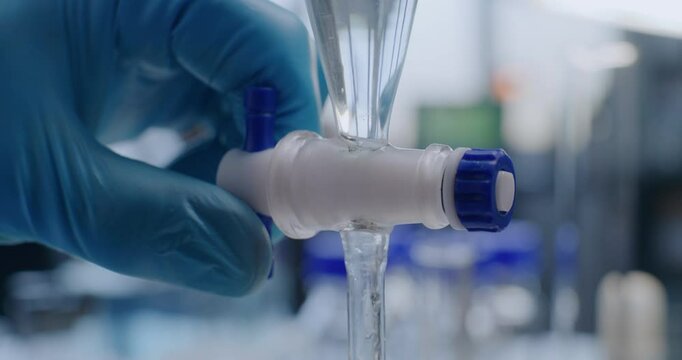 Equipped medical science laboratory: Close up of chemist opening stopcock on separating funnel, adding liquid. Professional scientist conducts chemical experiment using lab device. Chemistry concept.