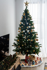 Beautifully decorated Christmas tree with golden ornaments, star topper, and festive miniature village at the base. Concept of cozy holiday decor, seasonal joy, and Christmas celebrations. High