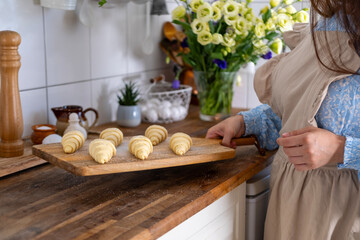 Unbaked raw croissants on wooden board, prepared for oven, held in woman’s hands, showcasing...