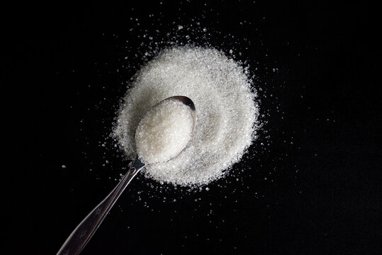 Fototapeta close up of poured white sugar with teaspoon on black background. concept of stop consume sugar for health