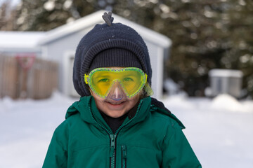 Young child is bundled up in winter clothes and wearing swim goggles while playing outside in the snow. Selective focus