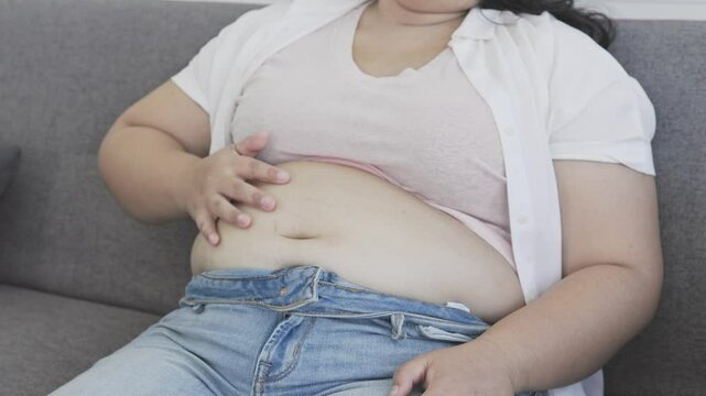 close up of chubby asian woman smacks her belly happily after eating food the pleasure of eating fat woman