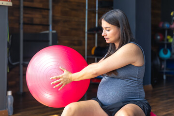 Fototapeta premium Pregnant sports woman with fit ball in the gym. The concept of sports lifestyle.