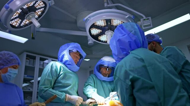 Four professional surgeons perform orthopedic surgery on trauma. Doctors in protective helmets operate patient's hip. Low angle view.