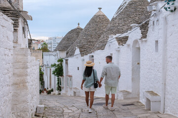 A couple strolls hand in hand through the picturesque trulli streets of Alberobello Puglia,...