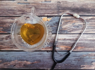 Heart shaped teacup with stethoscope on a wooden table, top view. Alternative medicine.