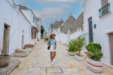 A traveler wanders leisurely along the picturesque cobblestone streets of Alberobello, surrounded...