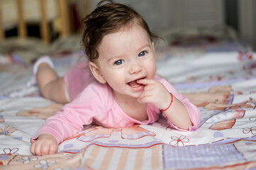 Baby or infant or small child or girl lying on her stomach looking at camera smiling and putting finger in mouth. Portrait of child with big blue eyes