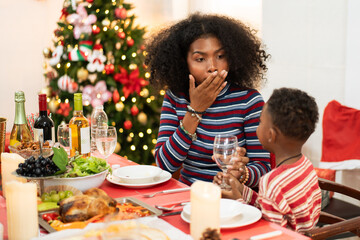 African family having Christmas dinner together at home. People drinking, eating and enjoy talking at dining table. Festive celebration party with delicious feast on holidays.