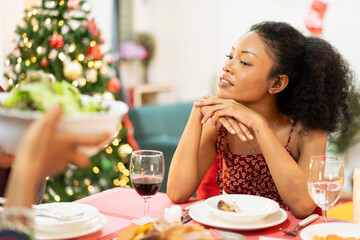 African family having Christmas dinner together at home. People drinking, eating and enjoy talking at dining table. Festive celebration party with delicious feast on holidays.
