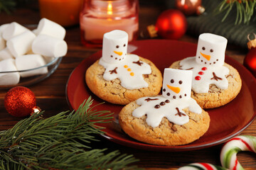 Funny marshmallow snowmen, cookies and festive decor on wooden table, closeup