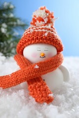 Cute decorative snowman on artificial snow against light blue background, closeup