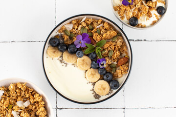 A healthy nutritious breakfast of natural Greek yoghurts, granola and fresh berries on tile background.