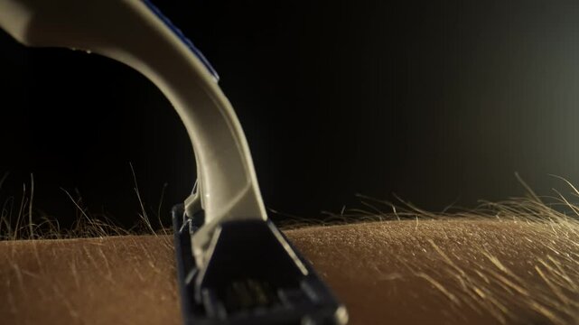 Macro shot of skin and hair texture. The razor passes over the hand and shaves off the hairs leaving behind bare skin.