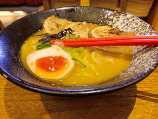 Miso tori paitan ramen with creamy savory chicken broth, grilled chicken slices and egg in black bowl isolated on wooden table.