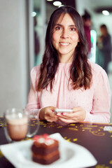 portrait smiling young latina woman sitting in a cafe holding smartphone