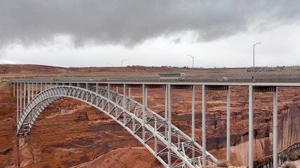 The historic Navajo Bridge in Arizona. Cars and a tour bus drive high over the Colorado River at Marble Canyon as storm clouds gather in the distance - USA