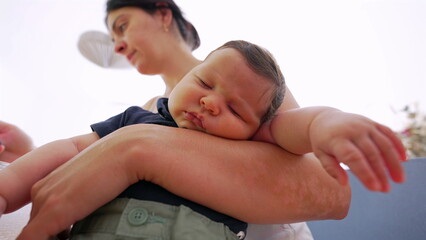 Baby sleeps soundly in a mother's arms, with the mother standing in a bright, airy space, reflecting the nurturing and serene environment of family life