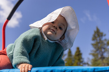 Baby girl wearing a sun hat is crawling on a trampoline on a sunny summer day. Selective focus