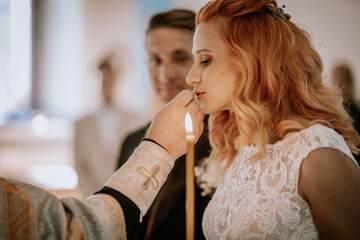 A woman receives a religious blessing, with a priest holding a candle in a traditional ceremony, highlighting faith and solemnity..