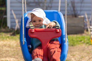 Adorable baby girl wearing a sun hat is having fun swinging outside on a swing set. Selective focus