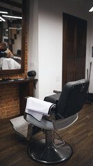 Empty barber chair with clean towel draped over armrest, awaiting client. Wooden floors and cozy...
