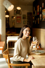 A joyful woman enjoying a glass of white wine while dining on a delicious meal at a trendy restaurant in the heart of the city
