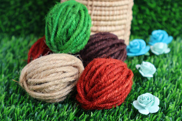 Rolls of hemp rope in assorted colors, green, red, cream, brown, placed on green artificial grass. Decorated with artificial flowers

