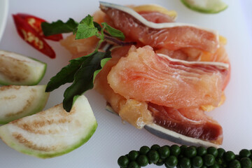 Sliced ​​fresh fish meat Place it in the middle between fresh pepper, brinjal, basil shoots, and red chilies, all on a white cutting board.