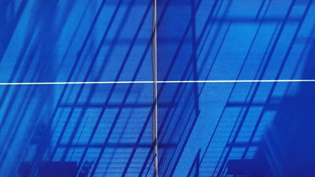 A blue paddle tennis court with shadows from the fence