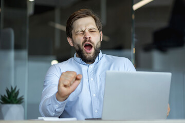 Tired office worker yawning in front of a laptop at work