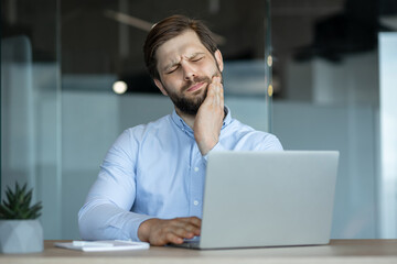 Businessman experiencing toothache while working on laptop in office