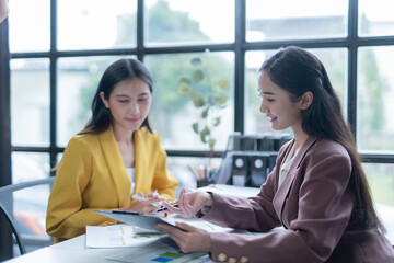 Two young businesswomen are having a productive meeting in a modern office, carefully examining financial reports and engaging in a collaborative discussion