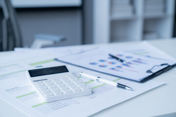 Calculator sitting on financial documents with charts and graphs, suggesting an accountant is...