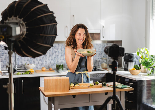 Food blogger smiling and showing pasta dish while recording cooking show