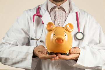 Close-up doctor holding a piggy bank in his hands, depositing money in a piggy bank, medical...