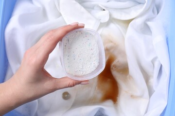 Woman adding powdered detergent into basin with dirty white clothes, top view