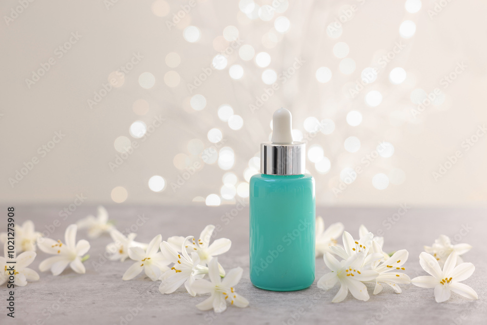 Sticker Cosmetic product in bottle and beautiful jasmine flowers on grey table against beige background with blurred lights