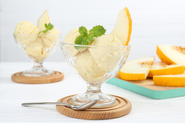 Scoops of melon sorbet with mint in glass dessert bowls and spoon on white wooden table, closeup