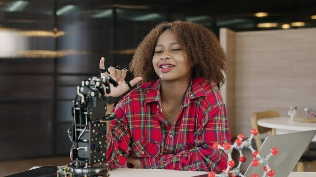 Happy African American teenage girl student with afro hairstyle learning and testing electronic technology of hand robotic for development of education intelligence futuristic skills in classroom. 