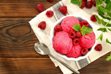 Delicious raspberry sorbet in bowl, fresh berries, mint and spoon on wooden table, flat lay. Space for text