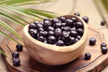 Ripe acai berries in bowl and palm leaves on wooden table, closeup