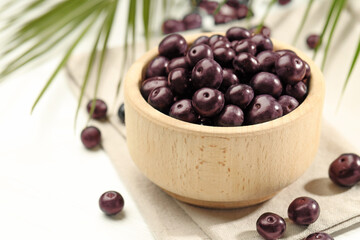 Ripe acai berries in bowl on white table, closeup