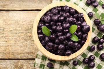 Ripe acai berries and leaves in bowl on wooden table, top view. Space for text
