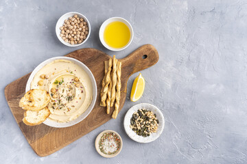 Hummus with olive oil in a gray ceramic plate. Toast and breadsticks for snacks. Top view, on a gray background.