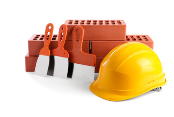 Yellow hard hat, red bricks and putty knives isolated on white. Building material and construction...